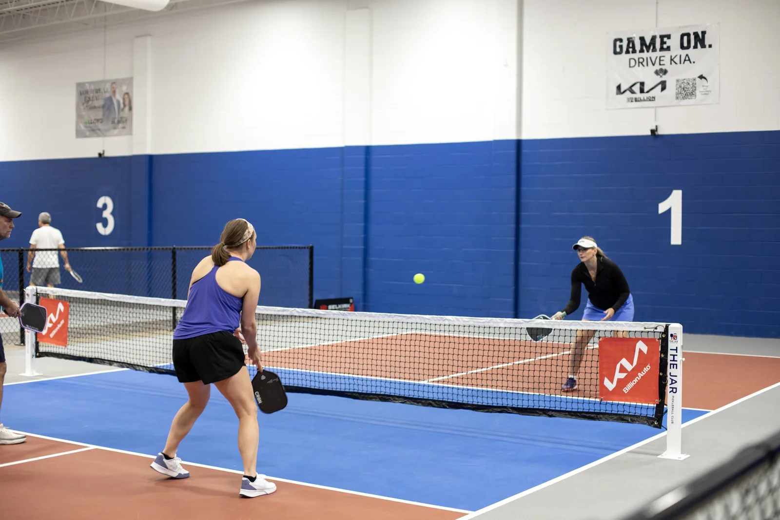 Players rallying across an indoor pickleball net